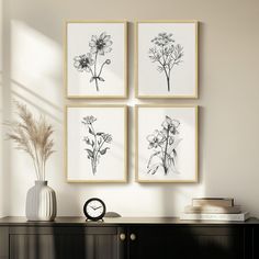 three black and white flowers are hanging on the wall next to a table with a clock