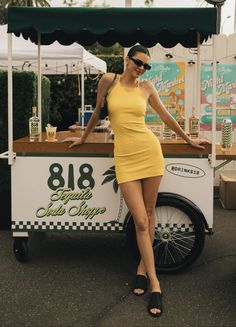 a woman in a yellow dress standing next to a food cart