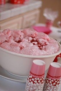 a white bowl filled with pink jello sitting on top of a table next to cups