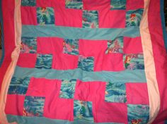 a pink and blue quilt with little mermaids on the side, sitting on a bed