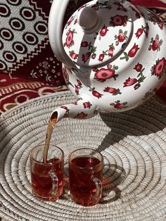 tea being poured into two cups on a wicker tray with red and white designs