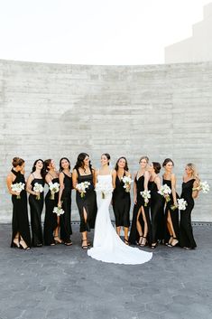 a group of women standing next to each other in front of a stone wall holding bouquets