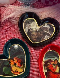 three heart shaped plates with paintings on them sitting on a red and white checkered tablecloth