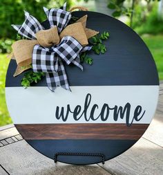 a welcome sign with a bow on it sitting on top of a wooden table outside