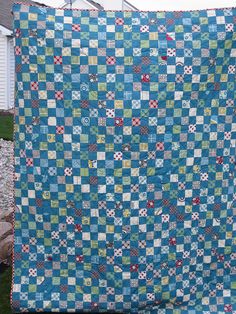 a blue and green quilt sitting on top of a grass covered field next to a house