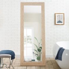 a bathroom with a white brick wall and wooden flooring is seen through a large mirror