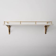 a white shelf with two brass brackets on it