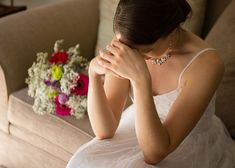 a woman sitting on a couch next to a bunch of flowers and holding her face