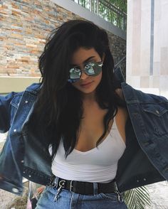 a woman in white shirt and blue jean jacket posing for the camera with sunglasses on