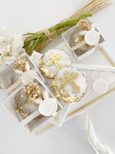 some white and gold decorated cookies in small boxes with flowers on the table next to them