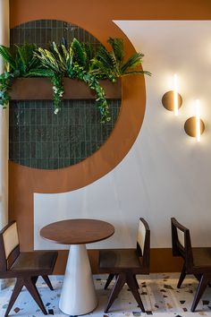 a table and chairs are in front of a wall with plants on it, along with two sconces