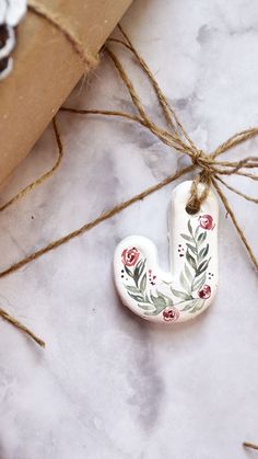 a ceramic letter with flowers on it tied to a brown paper bag next to some twine