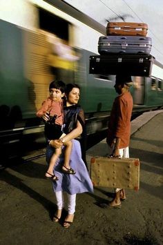 two women and a child are standing on the train platform with luggage strapped to their heads