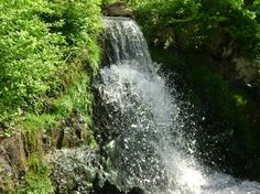 a small waterfall running down the side of a lush green hillside