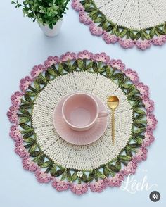 two crocheted placemats and a pink cup on a table with a gold spoon