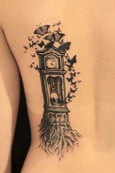 a woman's back tattoo with a clock and butterflies on her side, in black ink