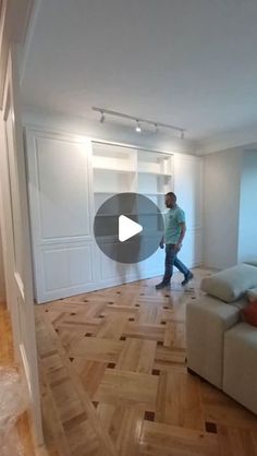 a man walking through a living room with hard wood flooring and white painted walls