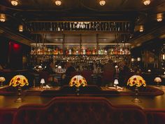 a dimly lit bar with red velvet couches and lamps on the wall behind it