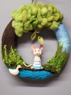 a felt ornament hanging on a wall with a mouse and tree in the middle