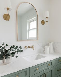 a bathroom with green cabinets and a white sink under a large oval mirror above it