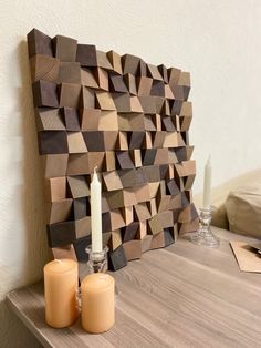 two candles are sitting on a table next to a wooden wall sculpture with geometric shapes