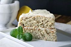 a piece of cake on a plate with a lemon and mint leaf next to it