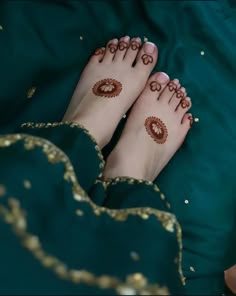 a woman with hendi on her feet laying down in green bed linens and gold sequins