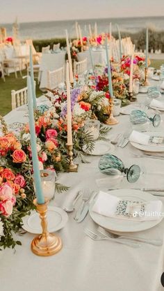 a long table is set up with flowers and candles for an outdoor wedding reception at the beach