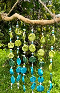 a green and blue wind chime hanging from a tree in front of some trees