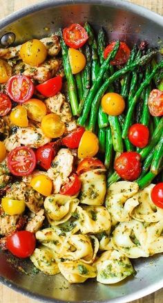 a pan filled with pasta, tomatoes and asparagus on top of a wooden table