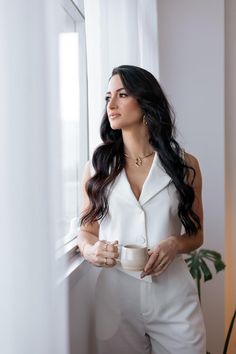 a woman standing by a window holding a cup