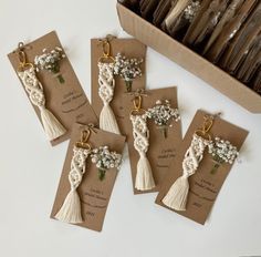 four tags with flowers and tassels on them sitting in front of a box