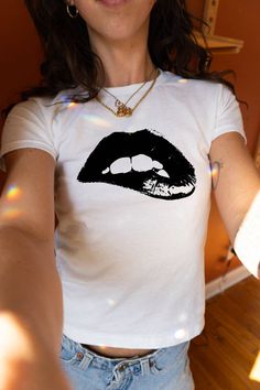 Introducing the Black Lip Baby Tee from PrintWithSky — your go-to piece for an effortless blend of style and comfort. Dazzle with this trendy Y2K-inspired top featuring a bold black lips graphic on a pristine white backdrop. Whether you're hitting the streets or just keeping it casual, this stylish streetwear top commands attention. It's designed to offer a perfect slim fit that accentuates your silhouette. Don't wait to add this must-have tee to your wardrobe. The model is wearing an XS size. O Outfit Ideas Grunge, Minimal Shirt Design, Tops For Women Casual, Trendy Shirt Designs, Workout Tops For Women, Graphic Print Shirt, Baby Graphic Tees, Black Lips, Streetwear Tops