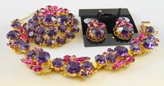 "DeLizza and Elster (aka D&E, Juliana) brooch, bracelet, and earrings demi parure in cardinal purple and fuchsia.  Cardinal in a bluer purple than amethyst purple, and is almost a deep tanzanite - absolutely beautiful, and combined with fuchsia is a knockout.  Set in goldtone, the brooch is done in cardinal rounds and fuchsia marquises and rounds, with amethyst rhinestone border around the center stone.  1 7/8\" in diameter, and 3/8\" deep.  The earrings are 1\" x 3/4\" and use the standard D&E 3-hole clip.  The 5 link bracelet uses the large cardinal rounds and fuchsia marquises (skinny navettes) and rounds, with the usual foldover clasp, linkage and safety chain, 7 1/4\" x 3/4\".  Excellent condition and completely gorgeous." Purple Brooch Jewelry For Evening, Luxury Pink Brooch Jewelry, Pink Evening Jewelry Brooch, Pink Evening Brooch Jewelry, Pink Brooch Jewelry For Evening, 1950s Bracelet, Juliana Jewelry, Antique Costume Jewelry, Diamond Wedding Sets