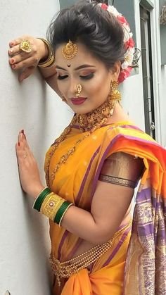 a woman in an orange and yellow saree leaning against a wall with her hands on her head