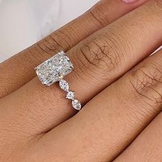 a woman's hand with a diamond ring on top of her finger and the other hand holding an engagement ring