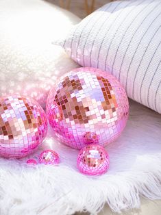 two pink disco balls sitting on top of a white blanket next to pillows and pillows