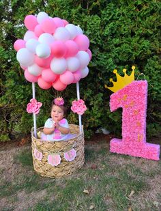 a baby in a basket with pink and white balloons next to the first birthday number