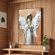 a painting of an angel with white wings on a wooden wall above a shelf and potted plant