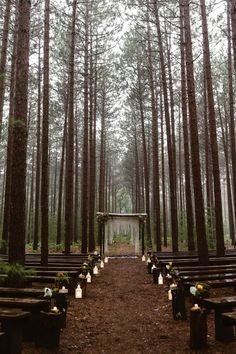 an outdoor ceremony in the woods with candles and flowers on benches lined up along the aisle