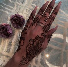 a woman's hand with henna tattoos on it and flowers in the background