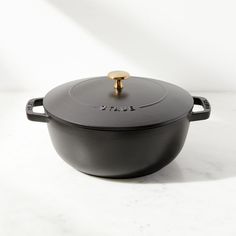 a black pot with a gold handle on a white surface