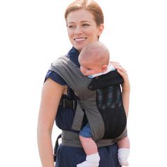 a woman carrying a baby in a carrier on the beach with water in the background