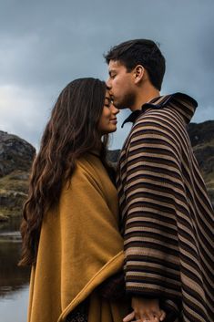 a man and woman standing next to each other in front of a body of water