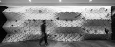 black and white photograph of a person walking in front of a wall made out of cubes