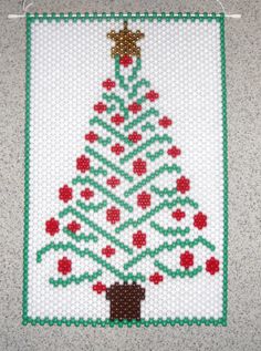 a cross - stitch christmas tree is hanging on the wall with red and green beads