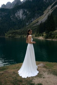 a woman in a white dress standing on the edge of a mountain overlooking a lake