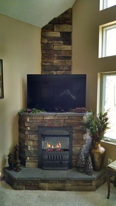 a living room with a stone fireplace and television on the mantle, surrounded by potted plants