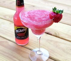 a pink drink sitting on top of a wooden table next to a bottle of booze