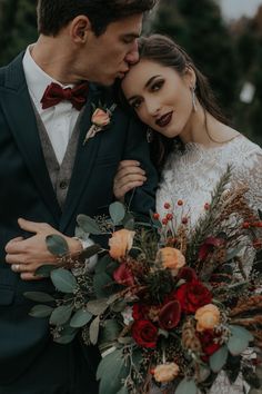 a man in a suit and tie kissing a woman with a bouquet on her shoulder